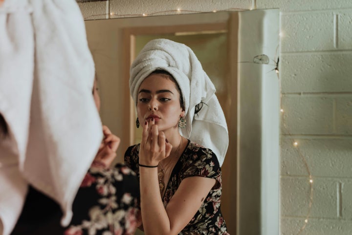 Teen applying skincare in bathroom mirror.