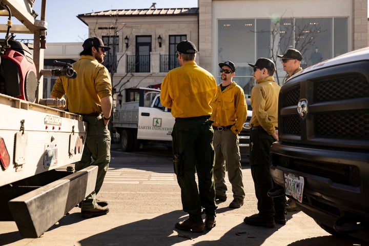 Private firefighting company employees, hired to protect Rick Caruso's Palisades Village shopping district from fire, gather near their vehicles on Wednesday.