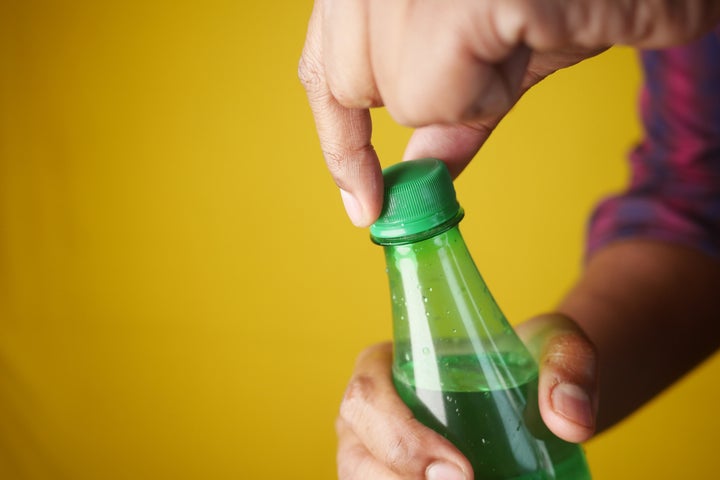 A person opens a green bottle cap against a bright yellow background, showcasing fun