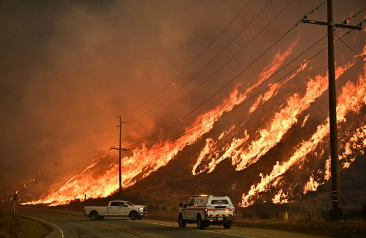 Emergency vehicles are on the side of the road as flames from the Hughes Fire race up the hill in Castaic, a northwestern neighborhood of Los Angeles, California, on January 22, 2025. A new wildfire erupted north of Los Angeles on January 22, exploding in size and sparking thousands of evacuation orders in a region already staggering from the effects of huge blazes. Ferocious flames were devouring hillsides near Castaic Lake, spreading rapidly to cover 5,000 acres in just over two hours. The fire was being fanned by strong, dry Santa Ana winds that were racing through the area, pushing a vast pall of smoke and embers ahead of the flames. Evacuations were ordered for 19,000 people all around the lake, which sits around 35 miles north of Los Angeles, and close to the city of Santa Clarita.