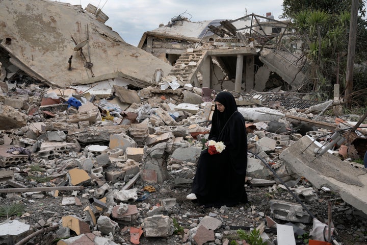 A Lebanese woman holds a bouquet of flowers as she sits on the rubble of a house destroyed by the Israeli forces, in the Aita al-Shaab village that sits on the Israeli-Lebanese border, on Sunday, Jan. 26, 2025.