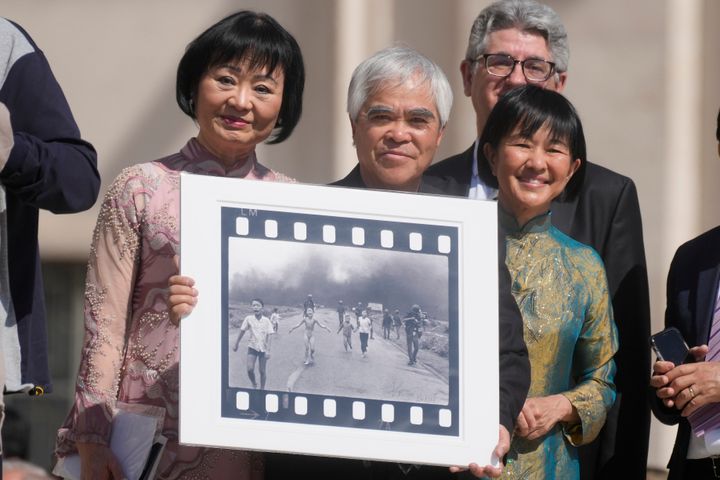 Pulitzer Prize-winning photographer Nick Ut, center, flanked by Kim Phuc, left, holds the "Napalm Girl", his Pulitzer Prize-winning photo, as they wait to meet with Pope Francis during the weekly general audience in St. Peter's Square at The Vatican in 2022.