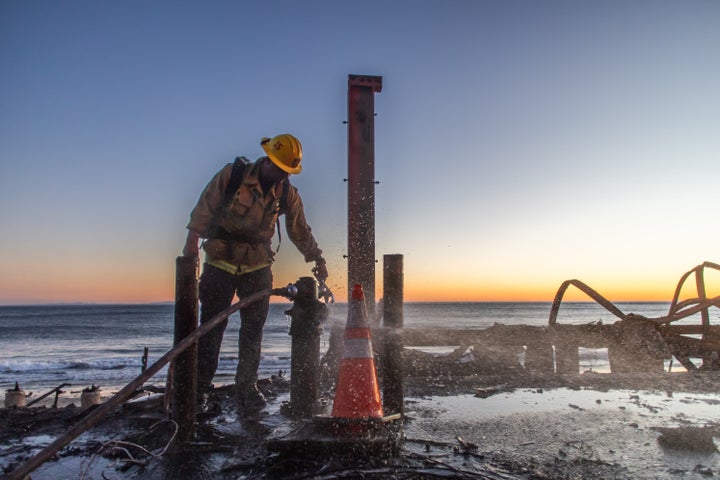 A firefighter tries to switch off a fire hydrant in front of a home at Pacific Coast Highway on Jan. 12 in the Pacific Palisades neighborhood of Los Angeles, California. Multiple wildfires fueled by intense Santa Ana Winds are still burning across Los Angeles County while some containment has been achieved. Over 12,000 structures have been destroyed in the fires.