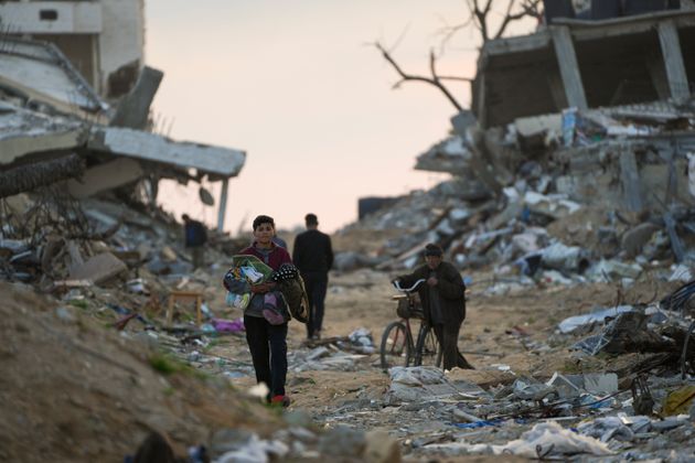 Palestinians walk along a street in Gaza City, littered with rubble from buildings destroyed during the Israeli army's ground and air offensive against Hamas in Gaza City, Tuesday Feb. 4, 2025.