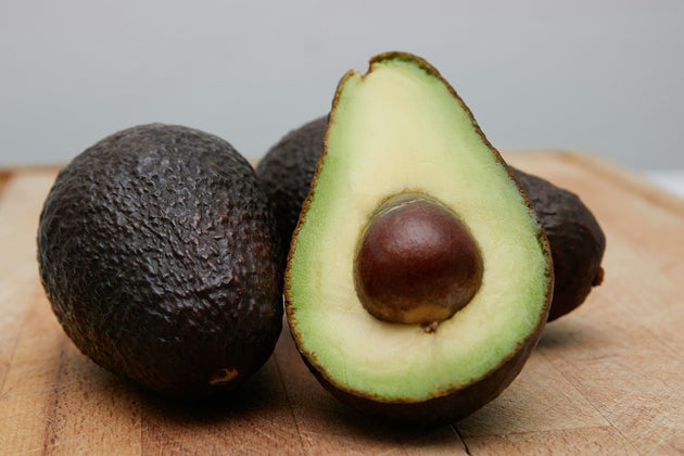 A halved avocado in front of two whole ones