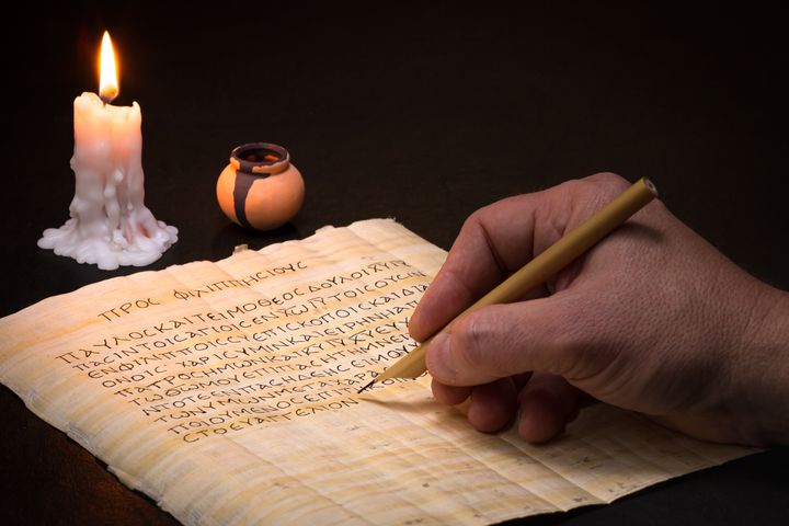 Scribe writing in Koine Greek on papyrus with a reed stylus by candlelight