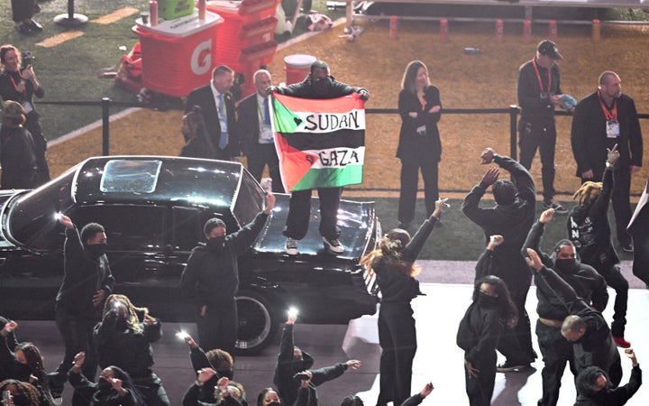 A protestor holds a flag with the words "Gaza" and "Sudan" as rapper Kendrick Lamar performs during the Super Bowl halftime show on Sunday, Feb. 9, 2025.