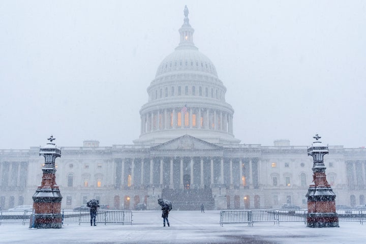 People sheltering with black umbrella's walk through snow at the Capitol, on Feb. 11, 2025, during a snowstorm in Washington.