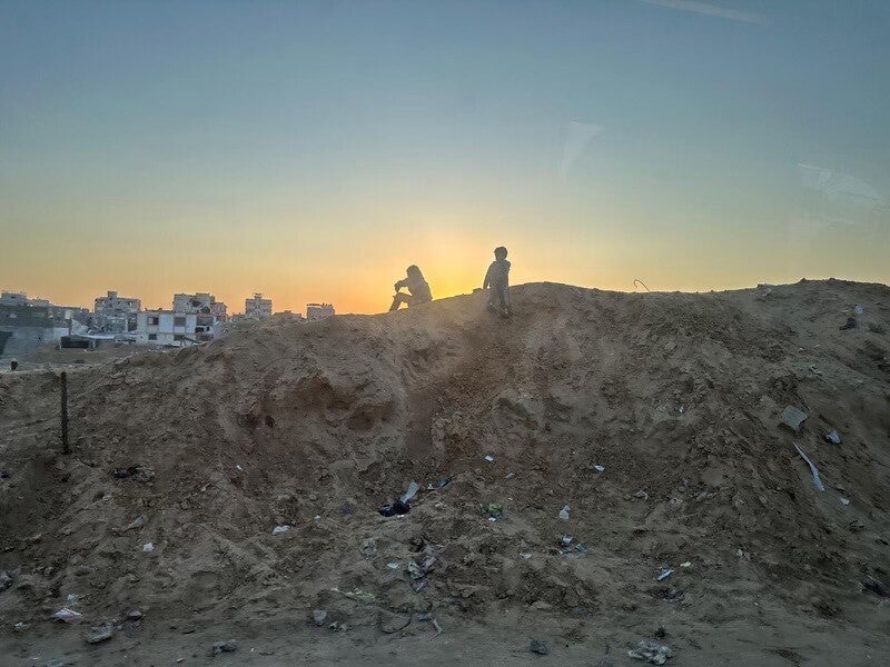 Two Palestinian youth sit on a mound in southern Gaza, following the Israel-Hamas ceasefire agreement.