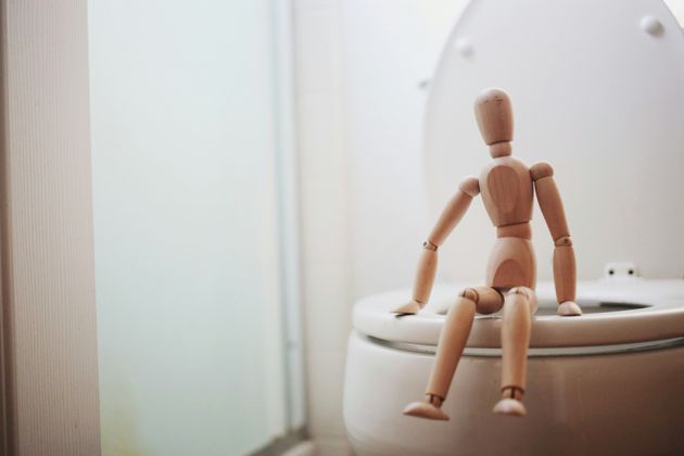 Wooden figurine seated on a loo seat