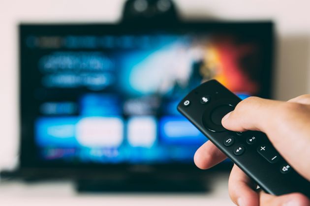 Hand holding a remote control in front of TV