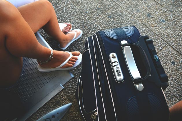 A person's feet in flip-flops beside a black suiitcase