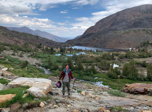 The author hiking just outside Yosemite National Park in July 2024, after cutting their hair short, holding their pink hat.