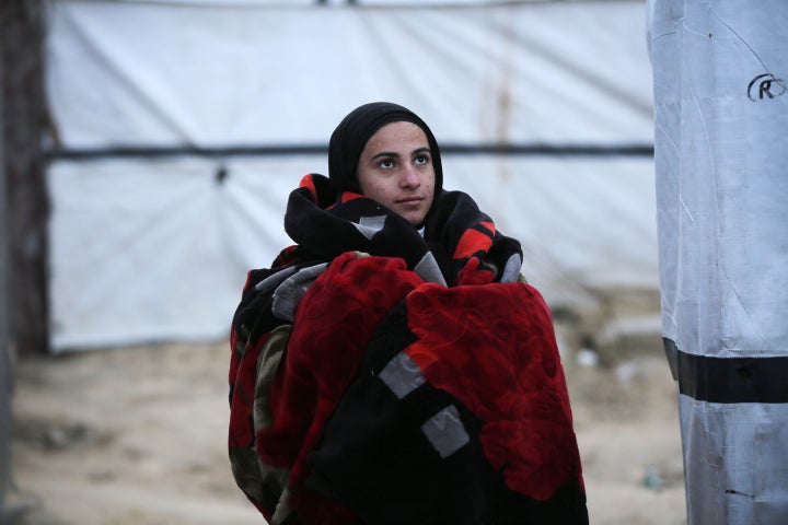 A Palestinian woman wraps herself in blankets to stay warm at a makeshift camp, as displaced families endure cold weather and difficult living conditions in Deir Al-Balah, Gaza, on Feb. 25, 2025.