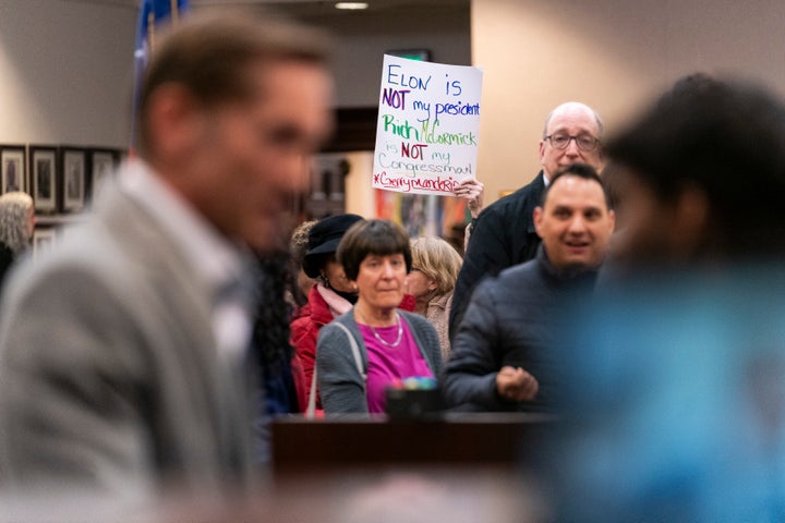 A town hall attendee holds up a sign referencing Elon Musk as Republican Rep. Rich McCormick speaks on Feb. 20, 2025, in Roswell, Georgia. 