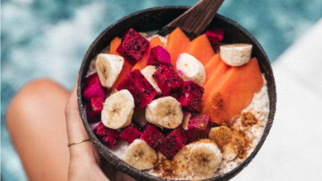 A fruit bowl with banana, papaya, coconut, and dragonfruit