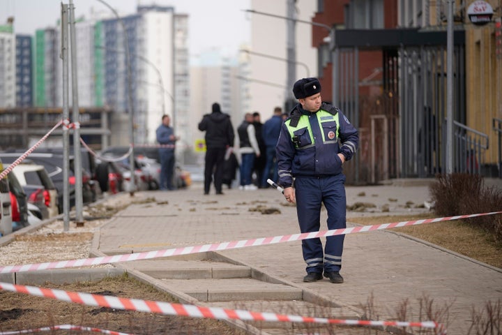 A police officer patrols an area near an apartment building, top, where a downed Ukrainian drone fell in Sapronovo village outside Moscow, Russia, on March 11, 2025.