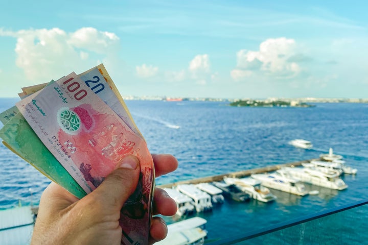 Male, Maldives - 7th may, 2024: tourist hand hold various currency maldivian notes in restaurant by harbor. Vacation expenses and Maldives business economy concept