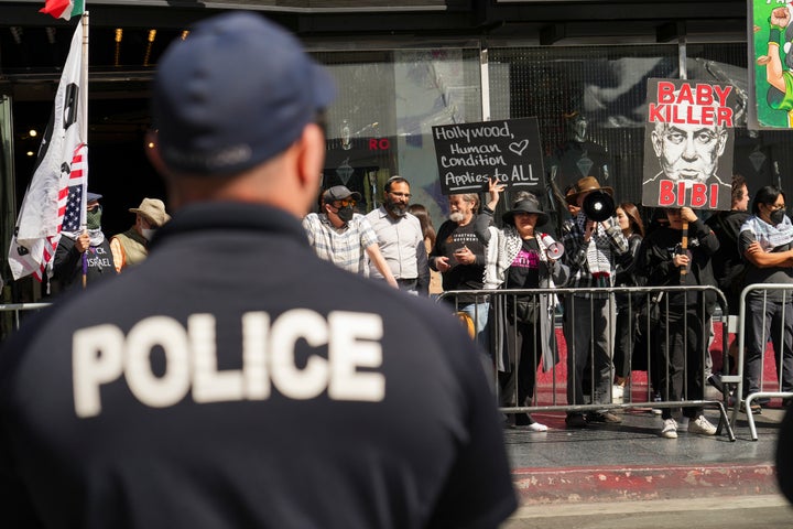 Police stand watch as people hold signs protesting the Israel-Hamas war prior to a ceremony honoring Gadot.