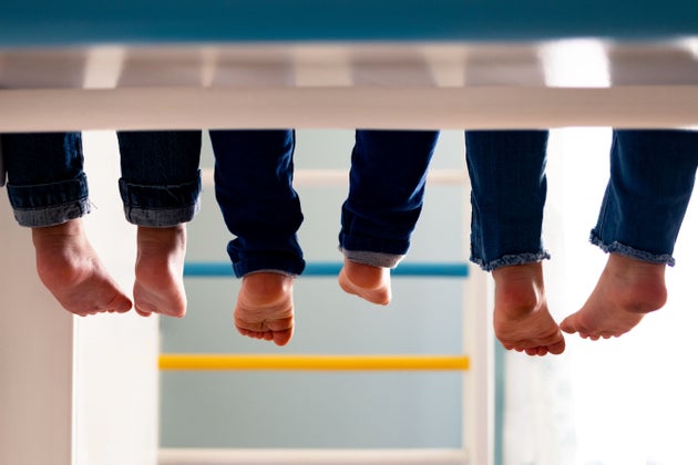 Ноги троих детей, сидящих на втором ярусе кровати, нижний ракурс.