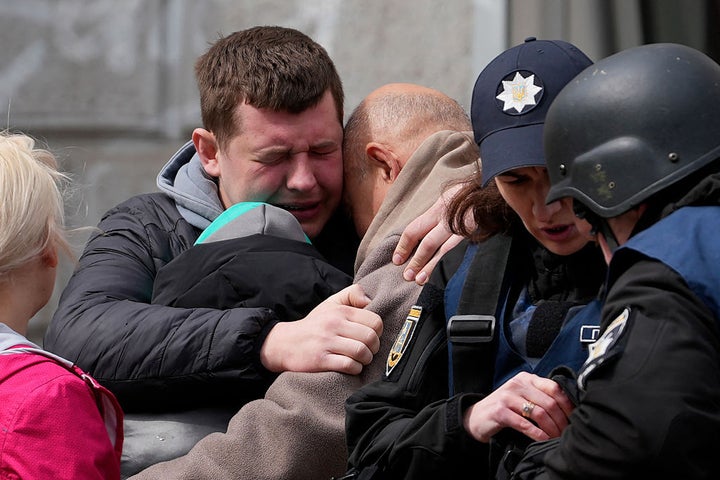 Two men comfort each other as Ukrainian police psychologists provide assistance to local residents following the missile attack.
