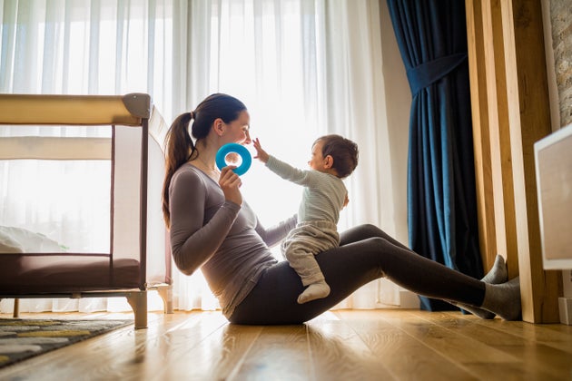 A mother and her baby enjoying playful bonding time on the floor in a cozy home setting.