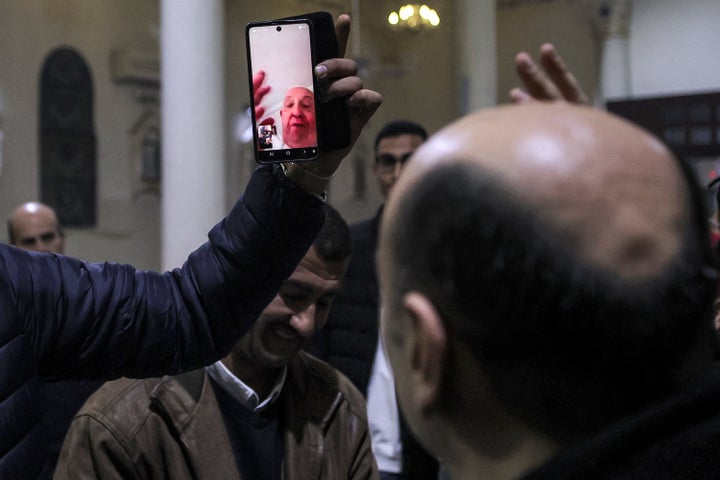 A man holds up a phone for the Rev. Gabriel Romanelli of the Holy Family Catholic Church displaying a video conference call with Pope Francis as the latter blesses the congregation during Christmas Eve Mass at the church in Gaza City in 2024.