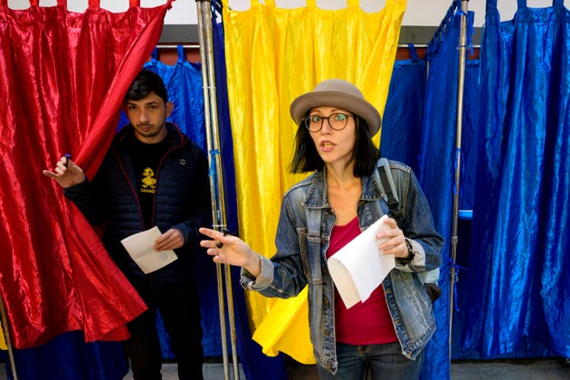 Άνθρωποι βγαίνουν από παραβάν ψηφοφορίας με τα χρώματα της ρουμανικής σημαίας ως κουρτίνες, πριν ρίξουν την ψήφο τους, στον δεύτερο γύρο των προεδρικών εκλογών της χώρας στο Βουκουρέστι της Ρουμανίας, Κυριακή 18 Μαΐου 2025. (AP Photo/Andreea Alexandru)