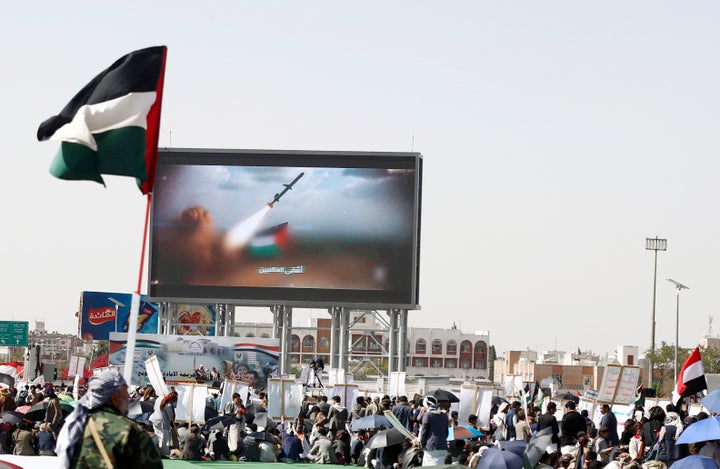 Yemenis sit by the Palestinian flag next to a screen broadcasting a missile launch by Houthi rebels, as they wait to protest Israel's continued bombardments and blockade in Gaza, on May 16, 2025 in Sana'a, Yemen.