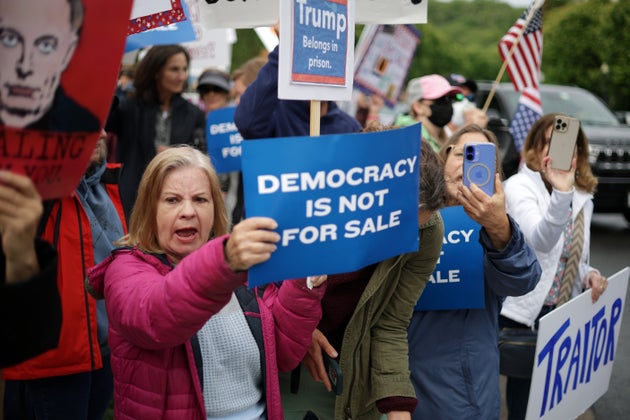 トランプ・ナショナル・ゴルフクラブの近くで「民主主義は売り物じゃない」と書かれた紙を掲げて抗議する人々（2025年5月22日）