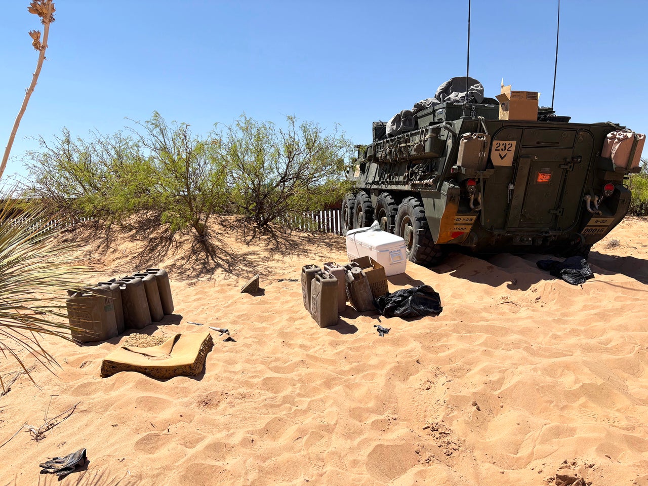 An armored Stryker vehicle faces the U.S.-Mexico border in Doña Ana County, New Mexico, with extra fuel canisters nearby.