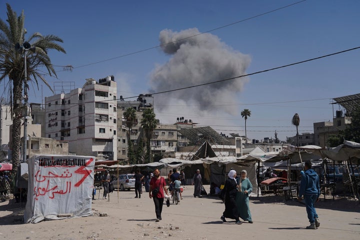 Smoke rises in the sky following an Israeli airstrike as Palestinians walk by a local market, in Gaza City, Friday, May 30, 2025. (AP Photo/Jehad Alshrafi)