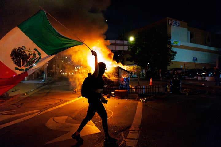 A demonstrator waves a Mexican flag in front of a dumpster fire after another night of unrest during a protest against immigration raids on June 8 in Los Angeles, California.