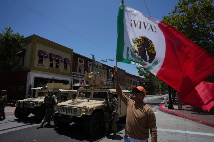 A protesters waves a flag standing by California National Guard parked along a street in Santa Ana, Calif. on Tuesday, June 10, 2025. (AP Photo Jae C. Hong)