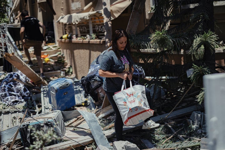 A woman carries belongings past rubble and debris in Rishon LeZion, Israel on June 14, 2025. An Iranian missile strike targeted the central city overnight, injuring several and causing widespread destruction according to Israeli authorities.