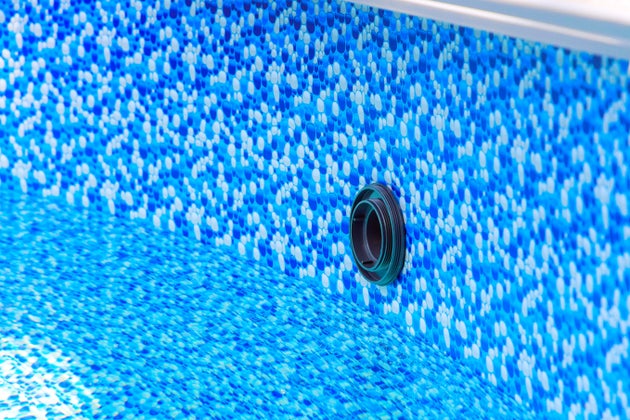 Bright blue mosaic design of pool liner reveals drainage opening in clear water