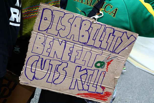An activist holds a banner against disability benefit cuts' during a protest by People's Assembly on June 7.