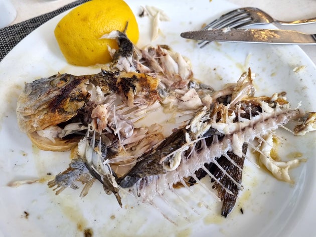 Close-up of fish skeleton and bones with lemon wedge on a white plate after eating