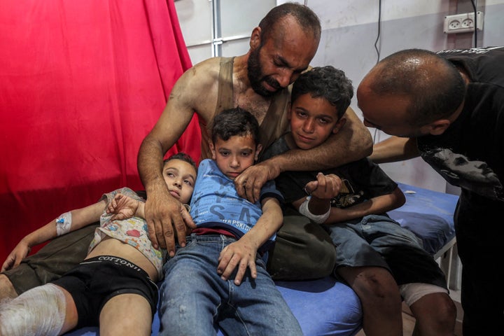 A man embraces three injured boys on a bed at the trauma ward of Al-Awda Hospital in central Gaza's Nuseirat camp, on July 6, 2025.