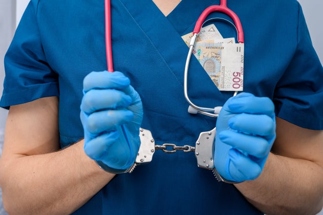 Doctor arrested, hands in police handcuffs close up