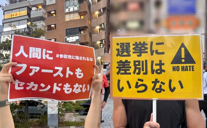 参政党の街頭演説で「選挙に差別はいらない NO HATE」「人間にファーストもセカンドもない」のプラカードを掲げる人たち