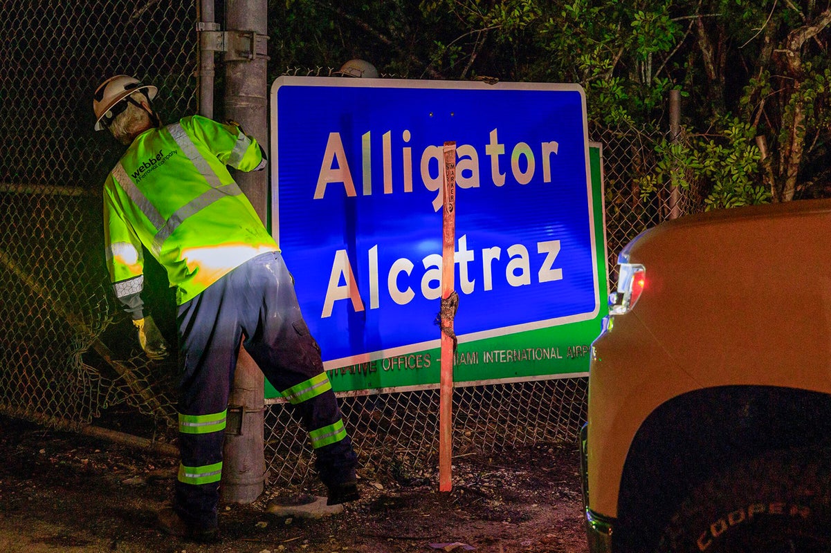Two workers finished covering the Dade-Collier Training and Transition Airport with the "Alligator Alcatraz," sign at the entrance of the migrant detention center, in Ochopee, Florida on Wednesday July 2, 2025. (Pedro Portal/Miami Herald/Tribune News Service via Getty Images)