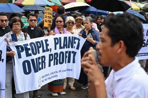 「利益より、人々や地球を優先せよ」との横断幕を掲げ抗議をする人々。