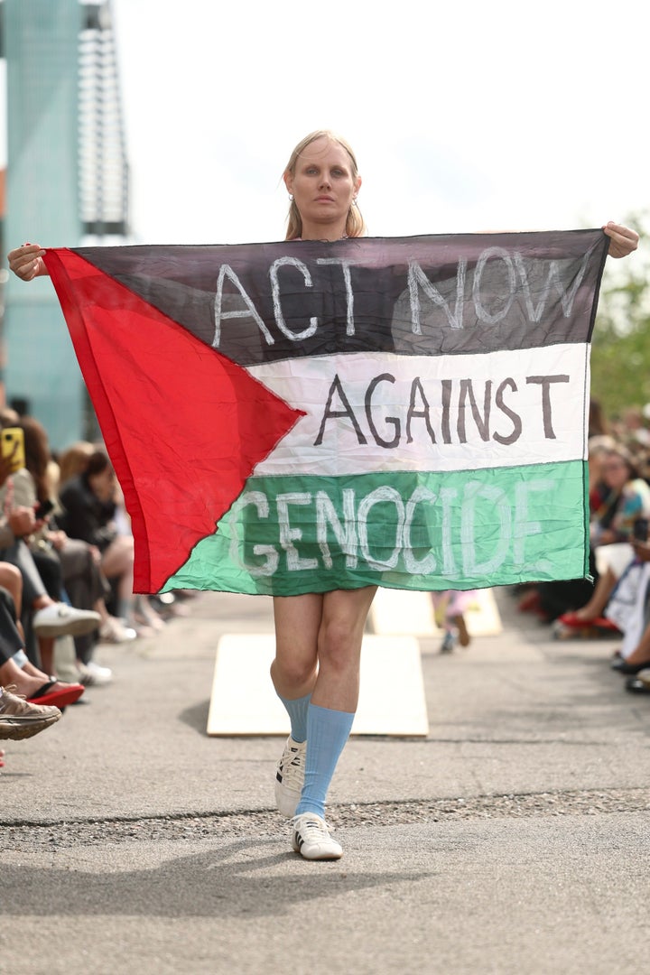 マリメッコのショーで、パレスチナの旗を掲げてジェノサイドに抗議しながらランウェイを歩くモデルのジュラさん(デンマークのコペンハーゲン、2025年8月7日)
