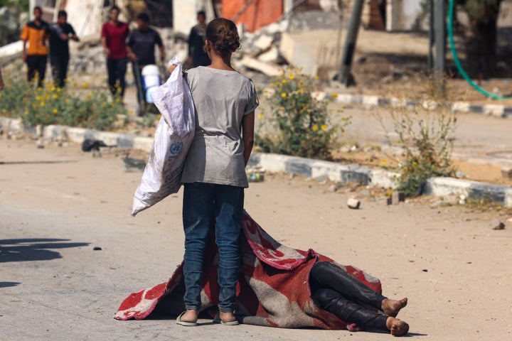Israel Kills 25 Assist-Seekers As Netanyahu Says He'll 'Enable' Palestinians To Depart Gaza 2 A Palestinian girl stands over the covered body of a person who was killed seeking food at a Gaza Humanitarian Foundation distribution point in central Gaza's Nuseirat camp, on Aug. 4, 2025.