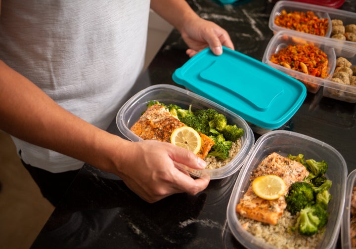 A person writing a meal plan on a notepad with fresh vegetables nearby.