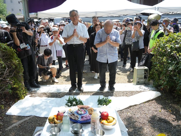 追悼碑に花を手向け、手を合わせる参列者