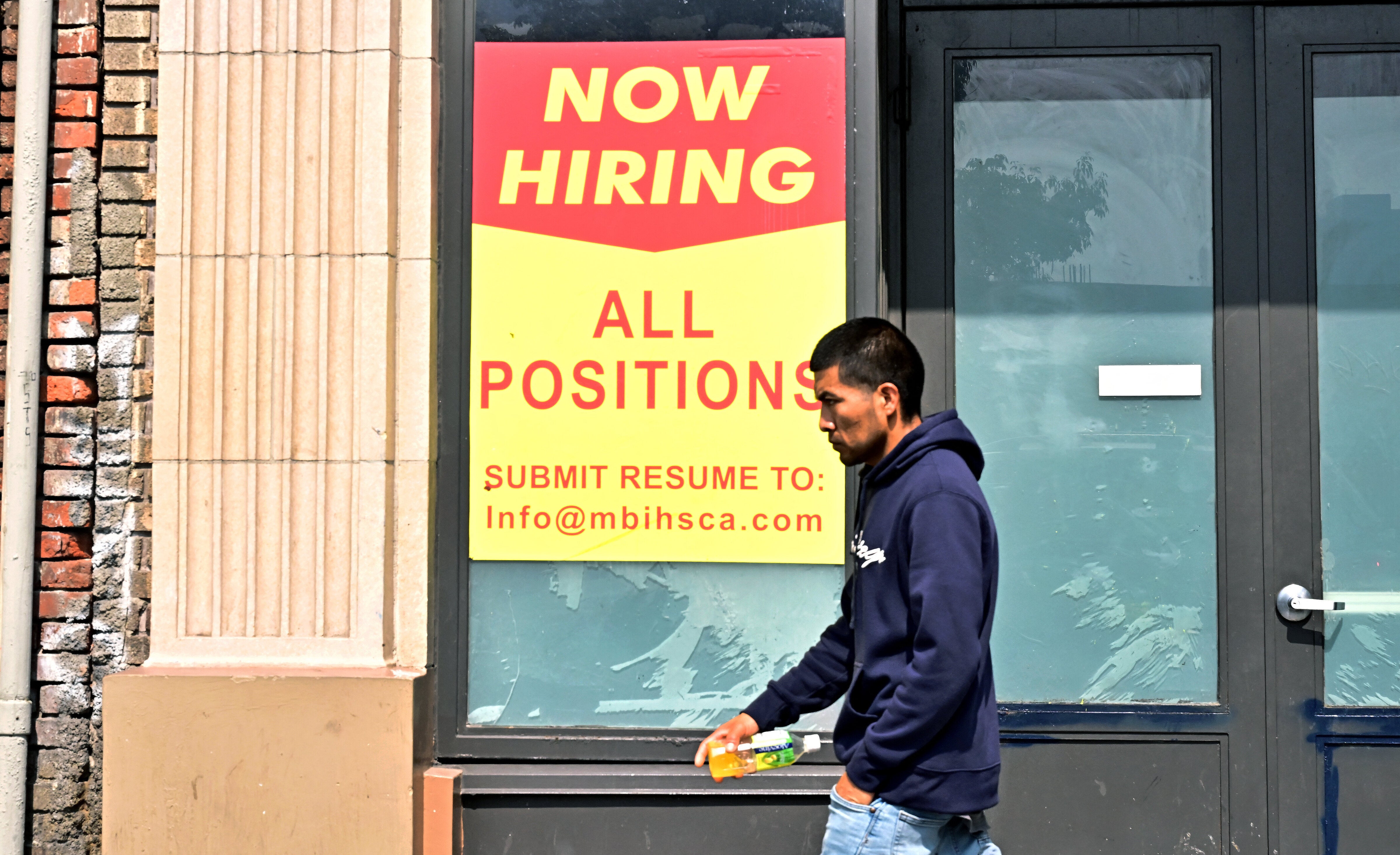 A pedestrian walks past a "Now Hiring" sign posted in front of a business in Los Angeles, California on August 13, 2025. (Photo by FREDERIC J. BROWN/AFP via Getty Images)