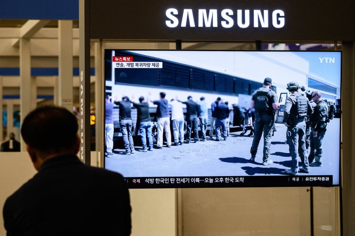 A man sits near a television at Incheon International Airport in Incheon on Sept. 12 that shows the news with file images of South Korean detainees standing against a bus during a raid by U.S. federal agents at a Hyundai-LG plant in Ellabell, Georgia.