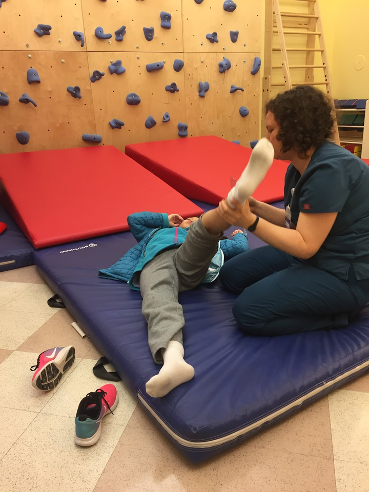 The author's daughter in rehab working with her PT on strengthening and stretching her lower extremities.